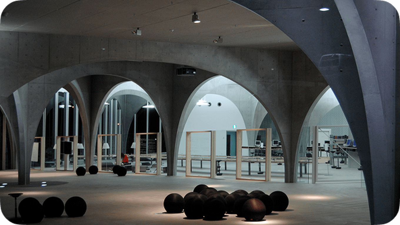 Modern interior with concrete arches, large windows, and scattered spherical objects on the floor, creating an open and minimalist atmosphere.