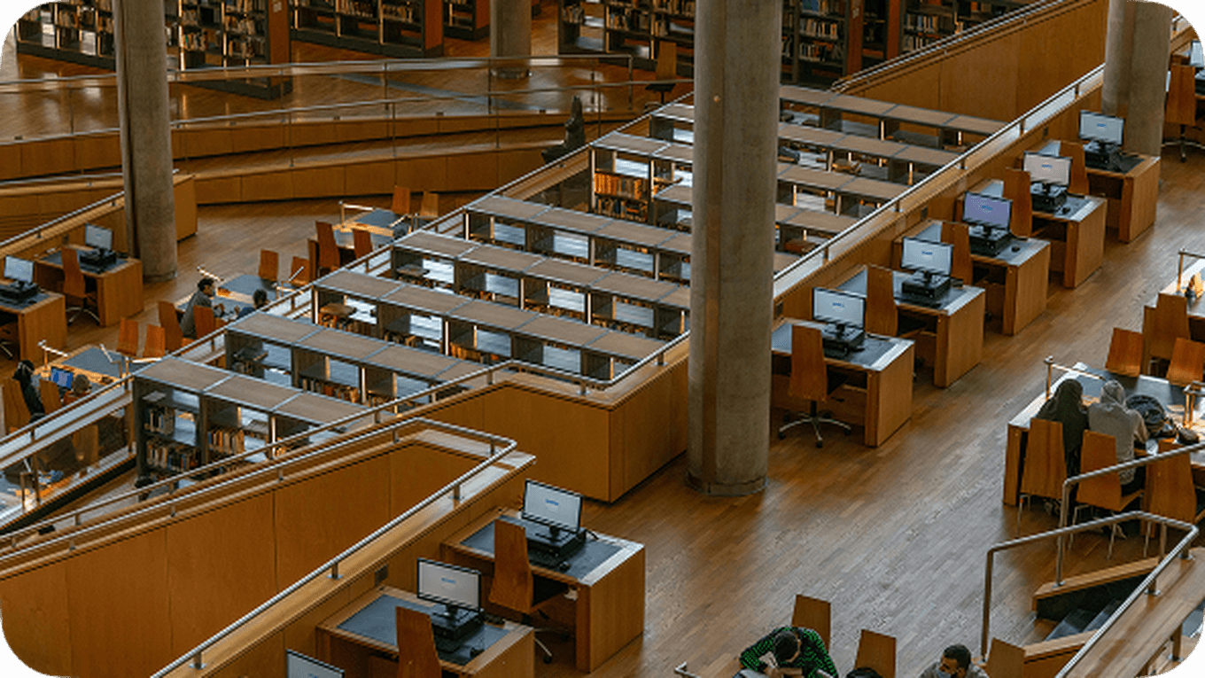A spacious library interior with multiple computer workstations, wooden desks, and bookshelves, viewed from above.