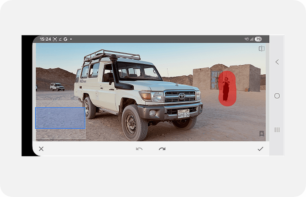 Smartphone photo of a white SUV parked on a desert road with mountains. A person stands near a building in the background.