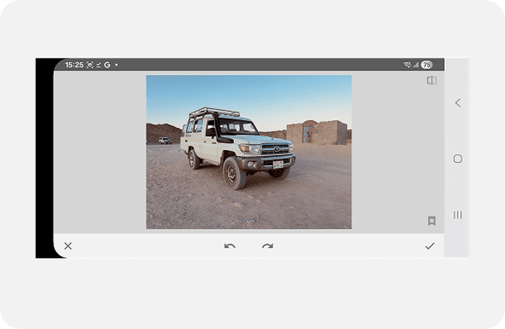 A white off-road vehicle parked on a desert landscape, with a clear sky and a building in the background, displayed on a smartphone screen.