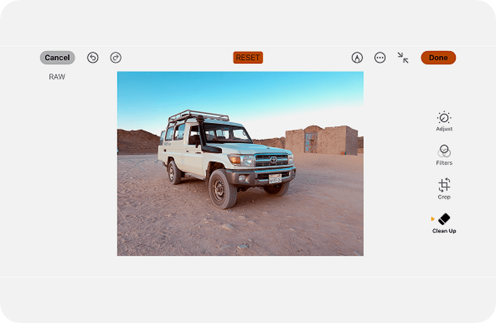 Editing interface showing a white off-road vehicle in a desert landscape. Options for adjusting, filtering, cropping, and cleaning up are visible.