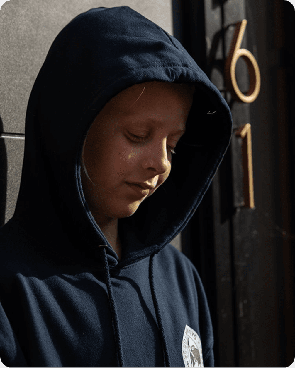 A person in a dark hoodie stands against a wall with the number 61, looking down thoughtfully.