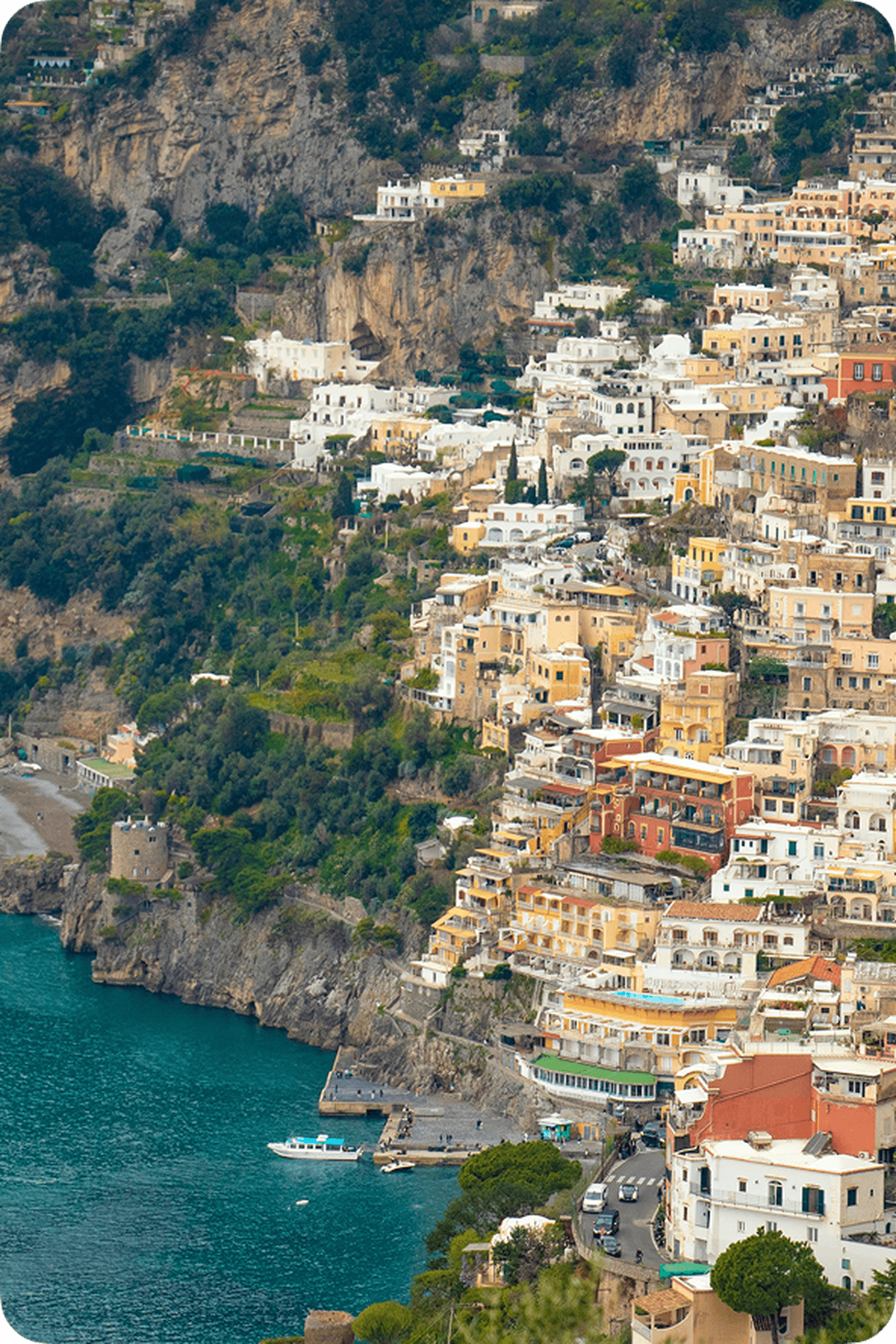 Colorful cliffside buildings overlook a turquoise sea in Positano, Italy, with a small beach and lush greenery surrounding the area.
