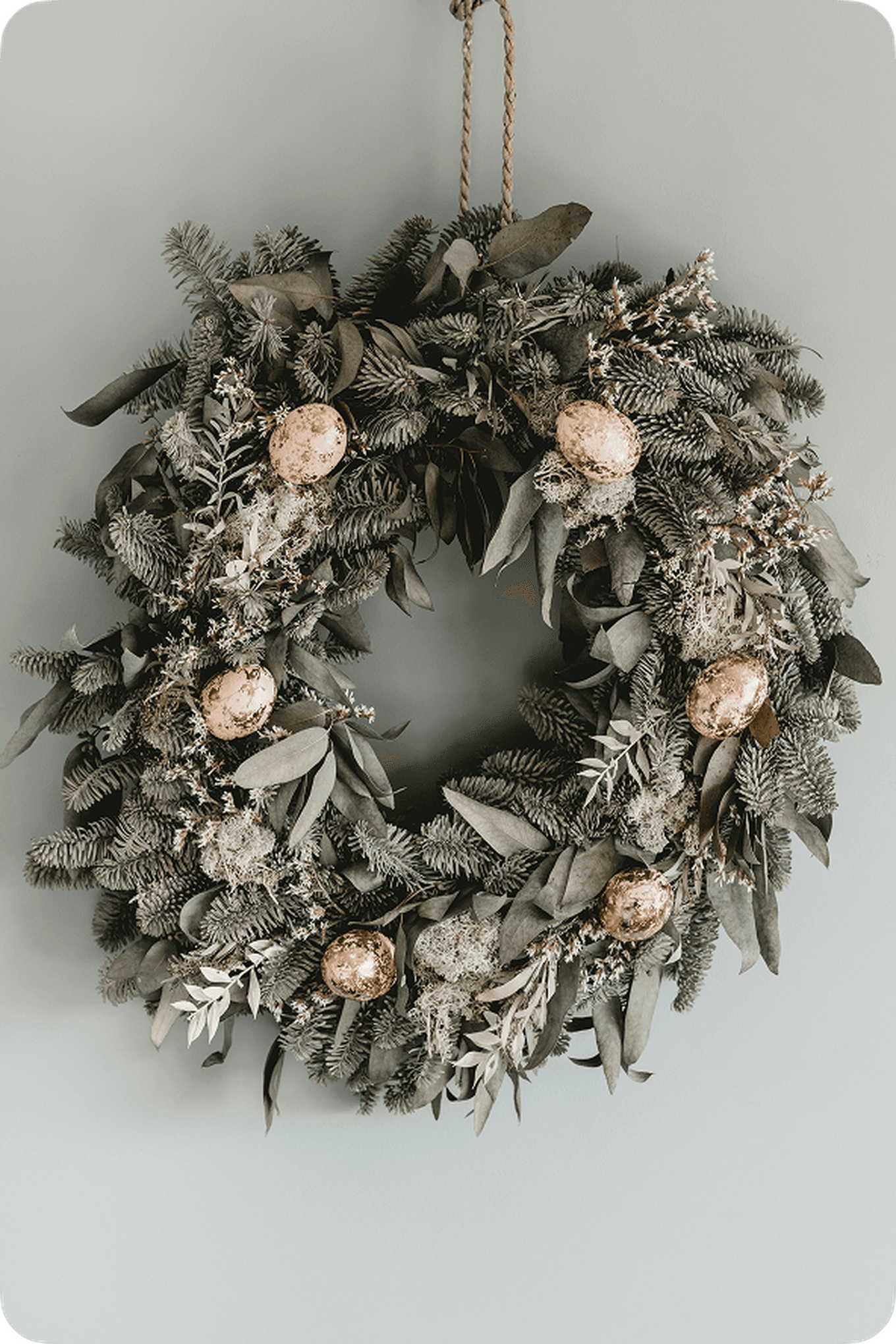 A decorative wreath with green foliage and gold ornaments hangs on a light gray wall.