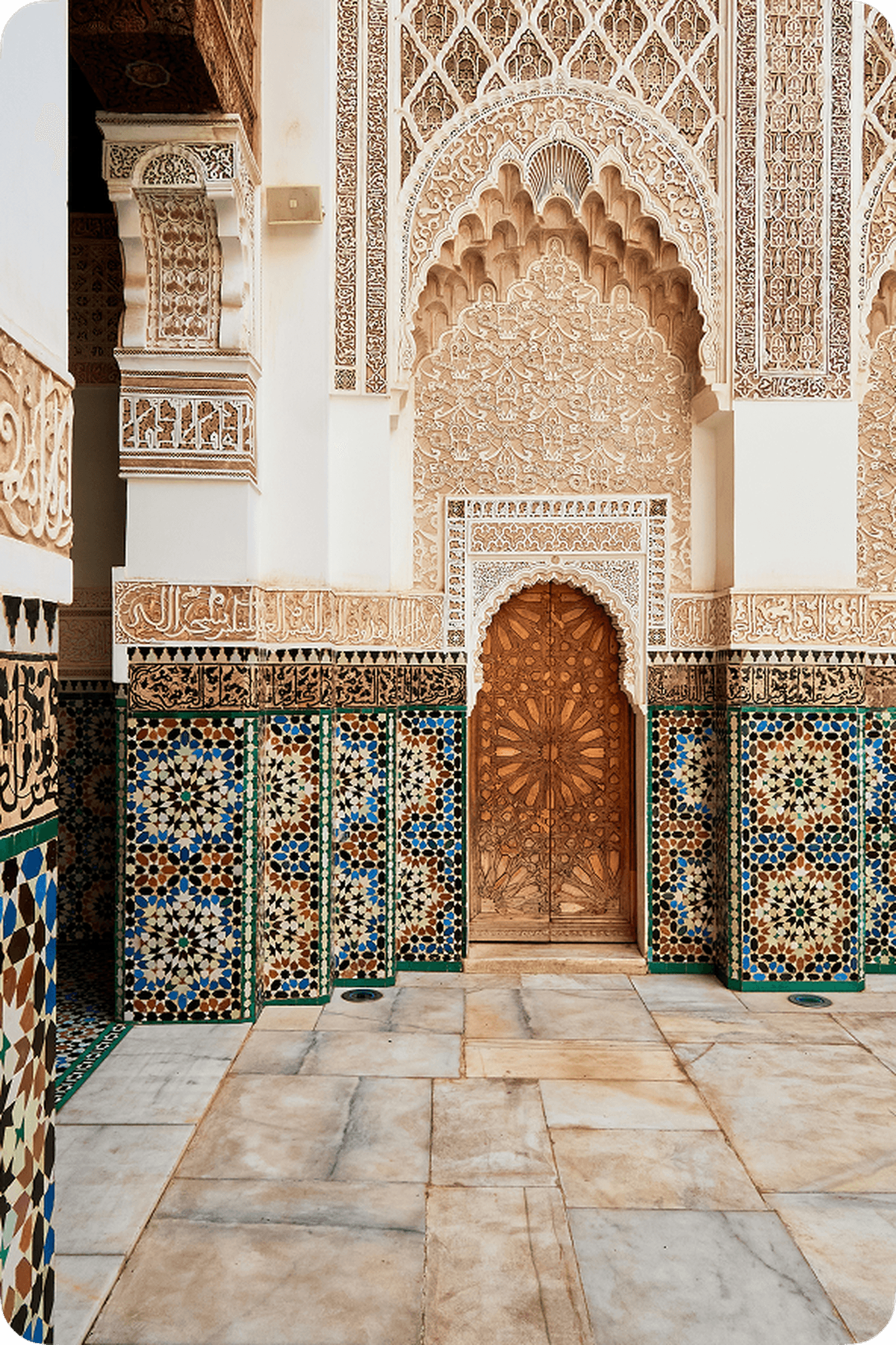 Ornate arched door with intricate carvings, surrounded by colorful geometric tiled walls in a historic building.