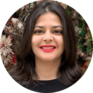 Smiling woman with long dark hair and red lipstick, standing in front of a floral background.