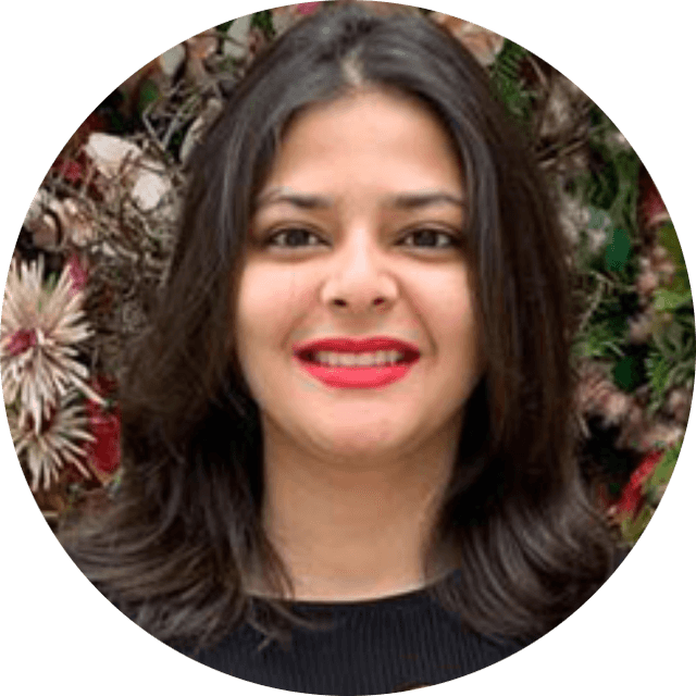 Smiling woman with long dark hair and red lipstick, standing in front of a floral background.
