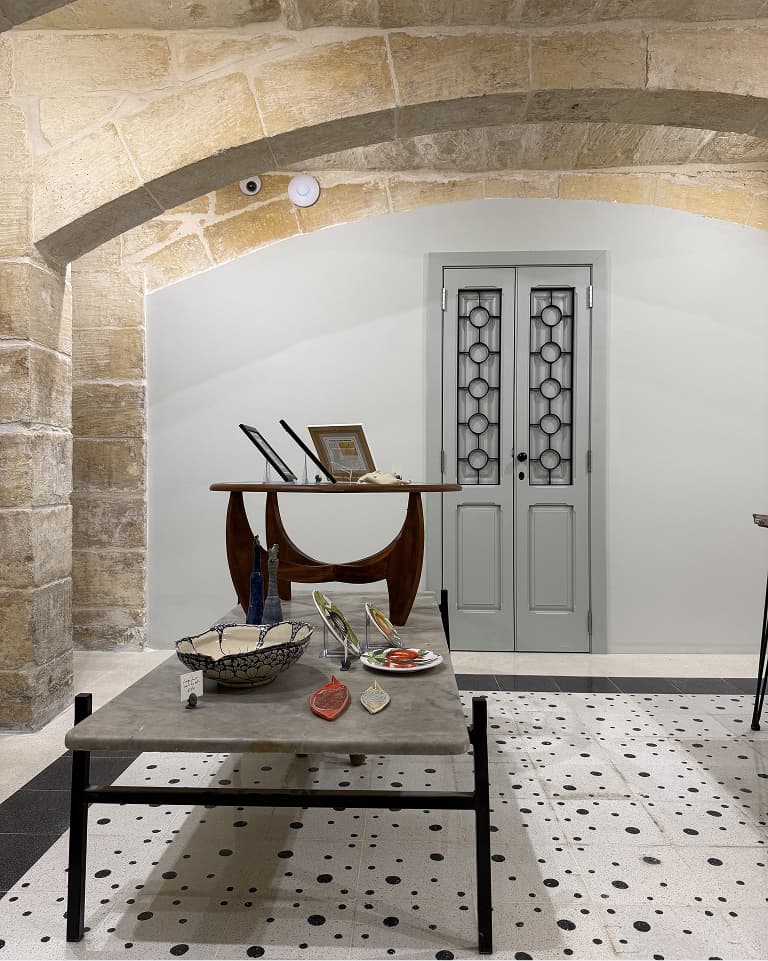 A stylish interior features stone arches, a table with decorative items, and a gray double door with circular patterns in the background.