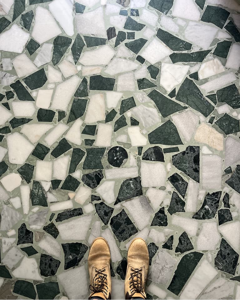 Beige shoes standing on a mosaic floor with irregular green and white stone tiles.