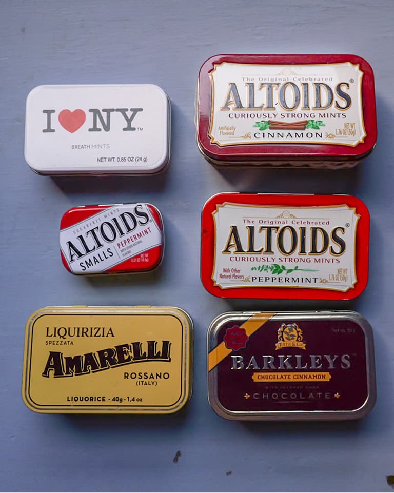Six assorted mint and candy tins (Altoids, I Love NY, Amarelli, Barkleys) arranged in a neat grid on a pale blue surface.