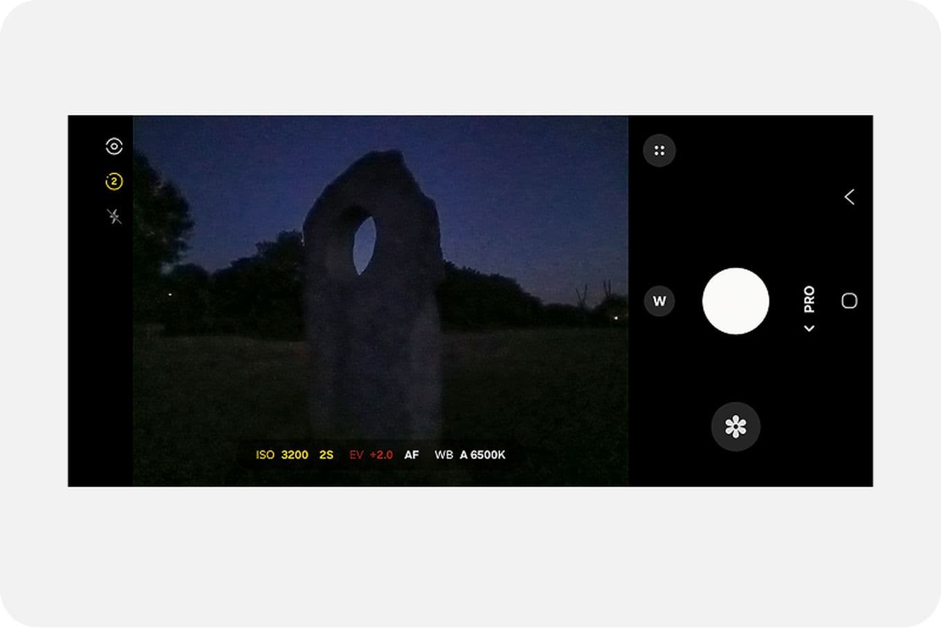 A smartphone screen displays a stone structure in a field at dusk, with camera settings visible on the interface.
