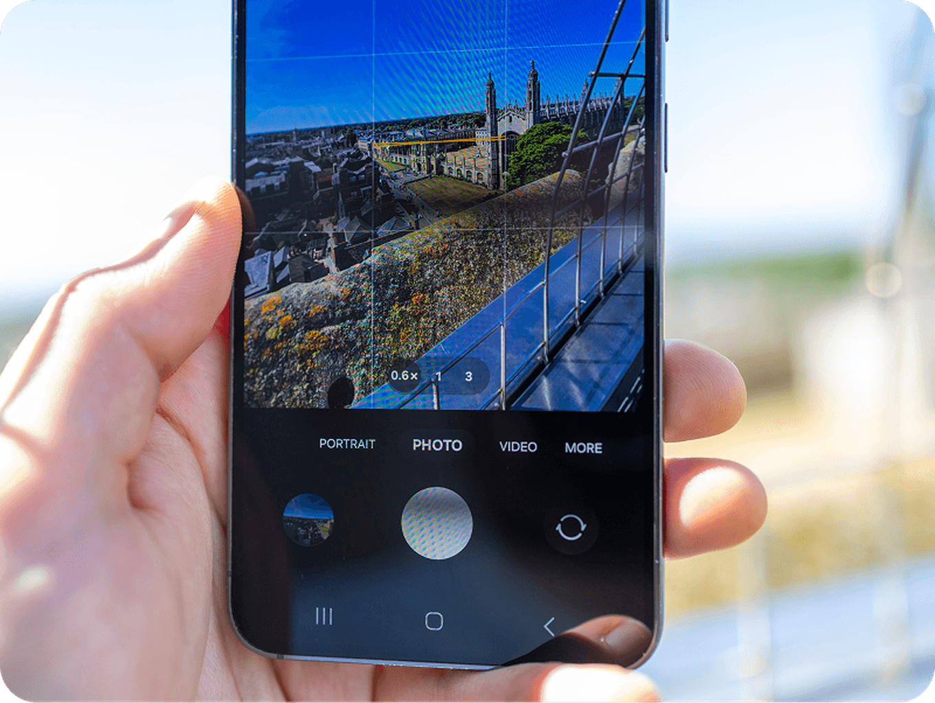 Close-up of a smartphone displaying a cityscape photo being captured, with a hand holding the phone. The screen shows camera settings.