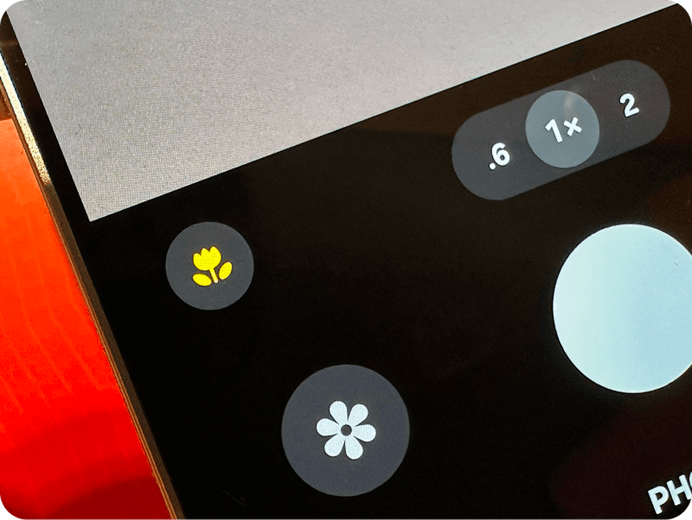 Close-up of a smartphone camera interface showing zoom options and flower icons, indicating different camera modes on a red surface.