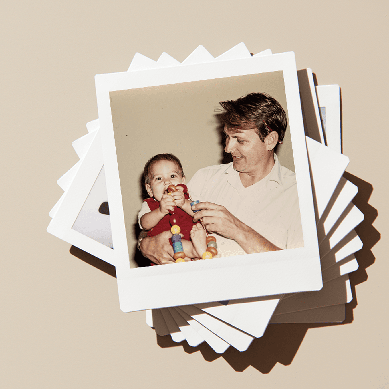 A stack of vintage photos, with the top photos showing a man holding a smiling baby with a toy