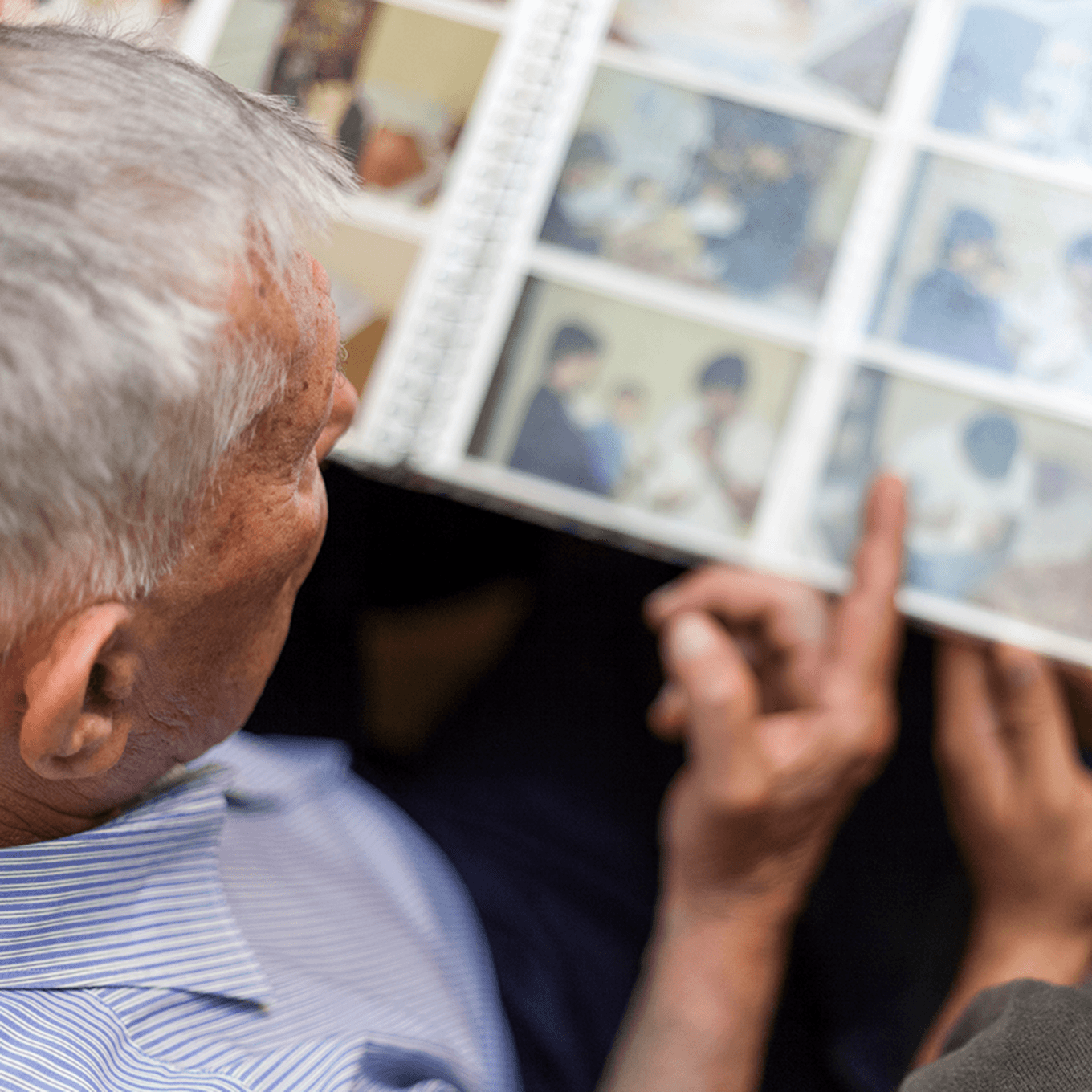Elderly man in a striped shirt looking at a photo album, viewing old photographs with blurred details.