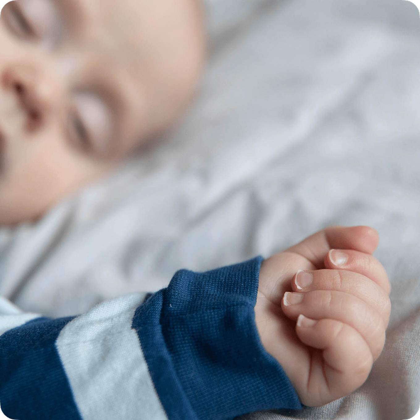 Sleeping baby in striped clothing with focus on their tiny hand resting on a soft blanket.