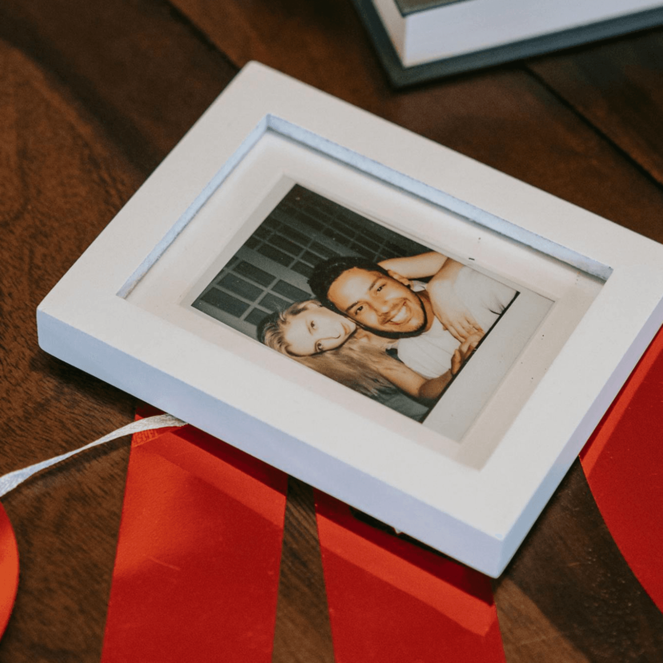 A framed photo of two people smiling, placed on a wooden table