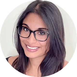 Close-up portrait of a smiling woman with long dark hair and black glasses against a light background.