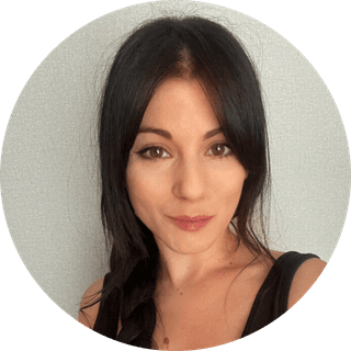 Woman with long dark hair in a braid, wearing a black top, smiling slightly against a neutral background.