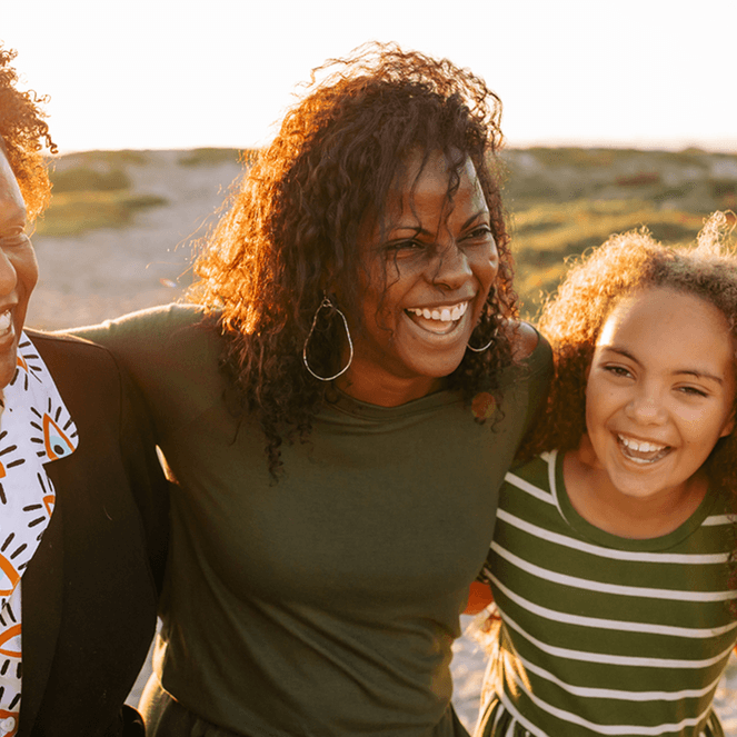 A mother, daughter and grandma smiling and hugging in a park setting