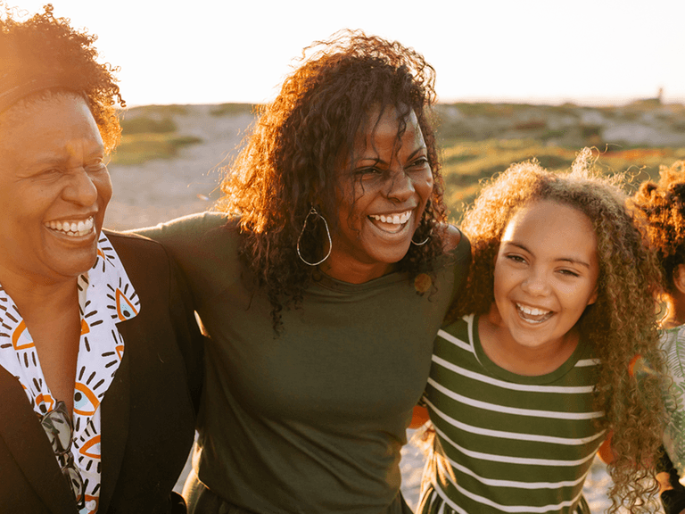 A mother, daughter and grandma smiling and hugging in a park setting