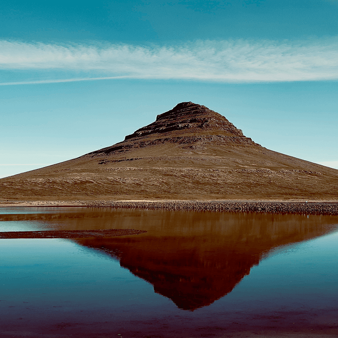 A conical mountain reflected in a calm lake under a clear blue sky, with a thin layer of clouds stretching horizontally.