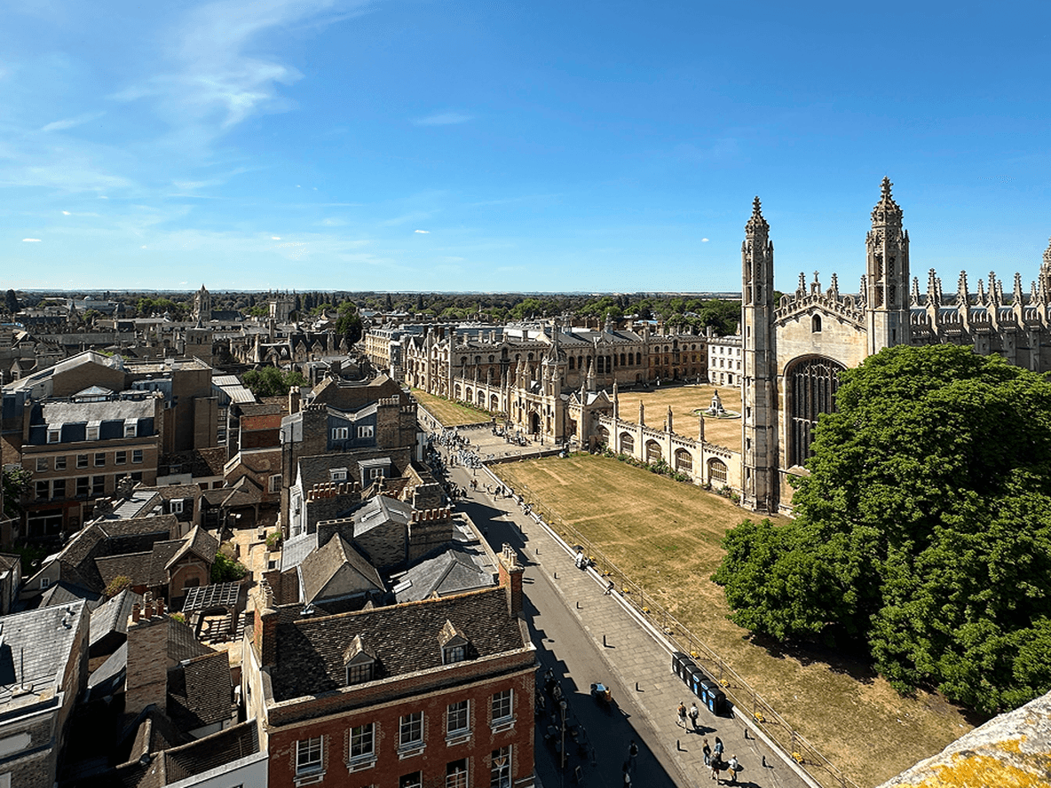 Aerial view of a historic city with a large Gothic-style building, tree-lined streets, and a clear blue sky.