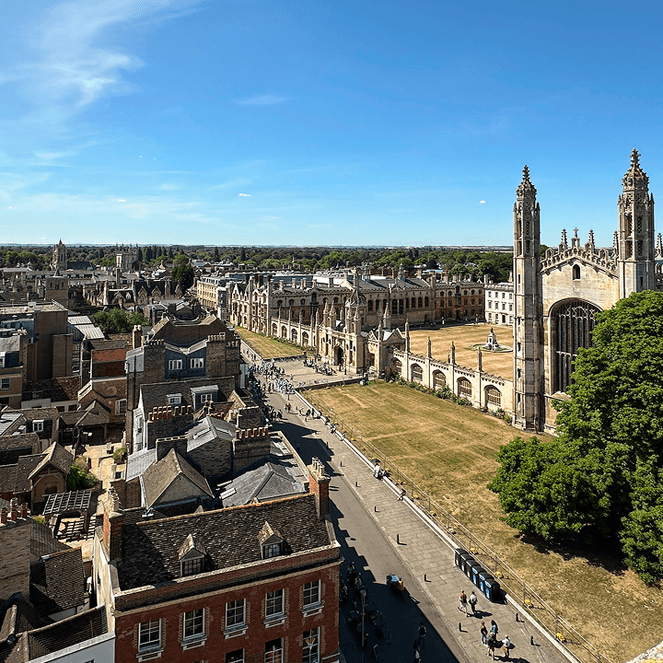 Aerial view of a historic city with a large Gothic-style building, tree-lined streets, and a clear blue sky.