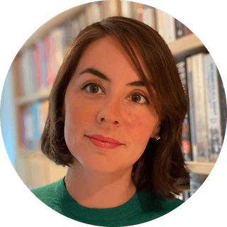 Woman with short brown hair and a green sweater, standing in front of a bookshelf filled with colorful books.