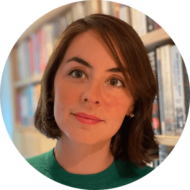 Woman with short brown hair and a green sweater, standing in front of a bookshelf filled with colorful books.