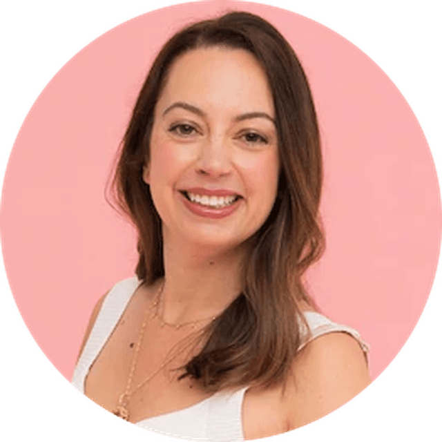 Smiling woman with long brown hair wearing a white top and necklace, set against a pink background.