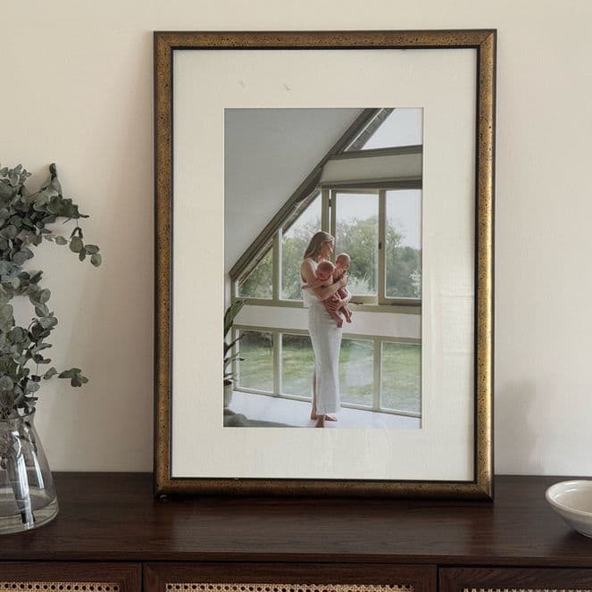 Framed photo on a wooden cabinet with a vase of greenery and a small bowl, against a plain wall.