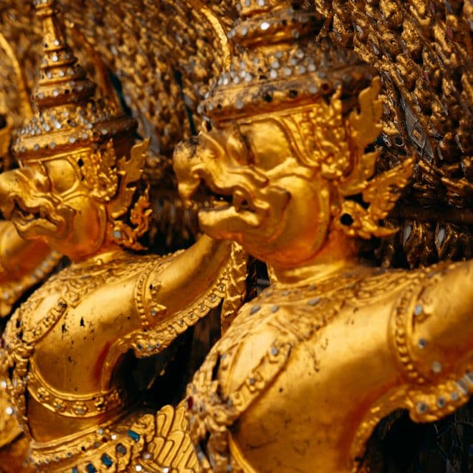 Close-up of gilded mythic guardian figures with ornate crowns and jewelry carved in a row on a temple facade.