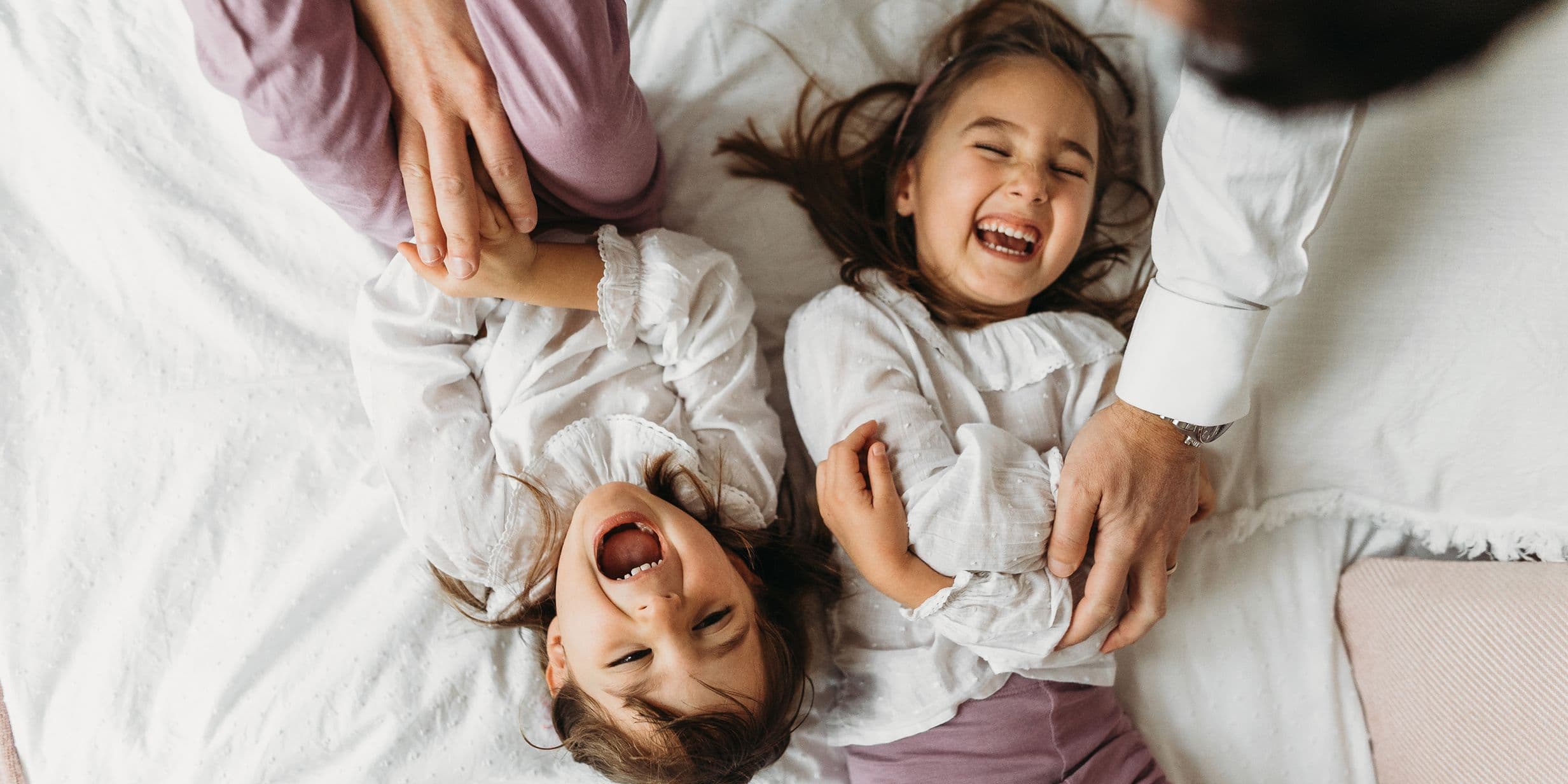 Young sisters giggling and squirming while being tickled by their parents on a bed