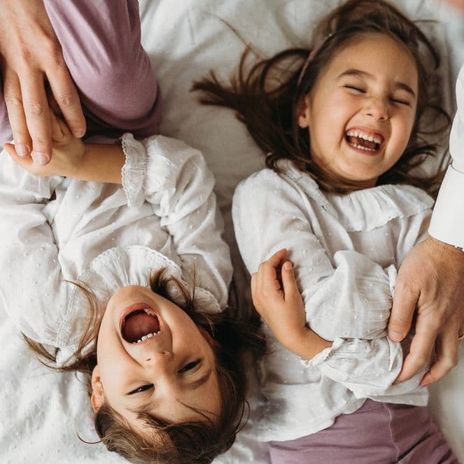 Young sisters giggling and squirming while being tickled by their parents on a bed