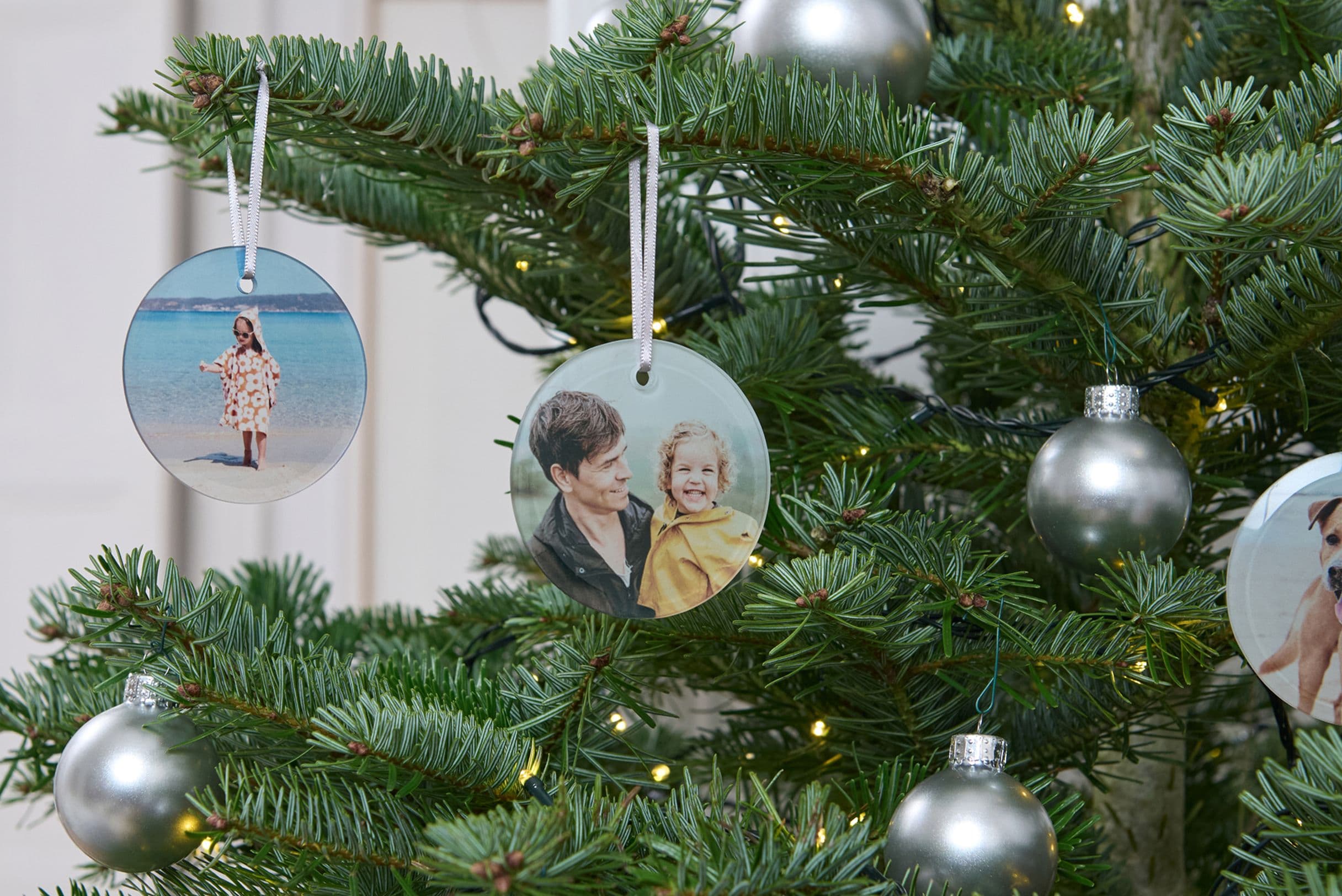 Christmas tree with silver baubles and personalized photo ornaments featuring people, a child, and a dog.