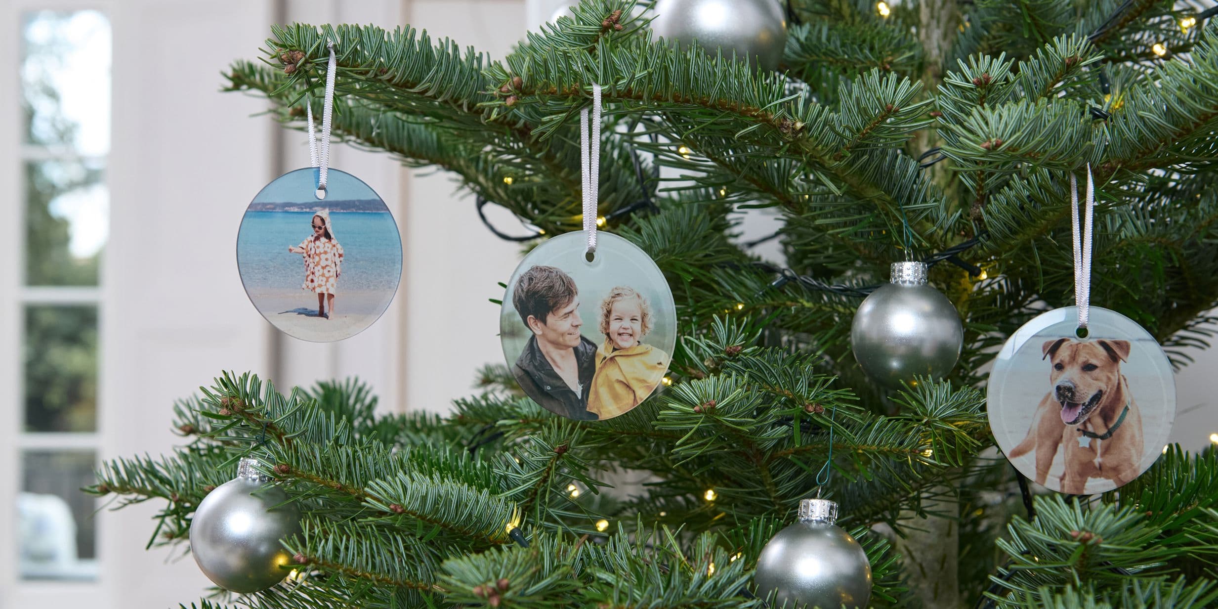 Christmas tree with silver baubles and personalized photo ornaments featuring people, a child, and a dog.
