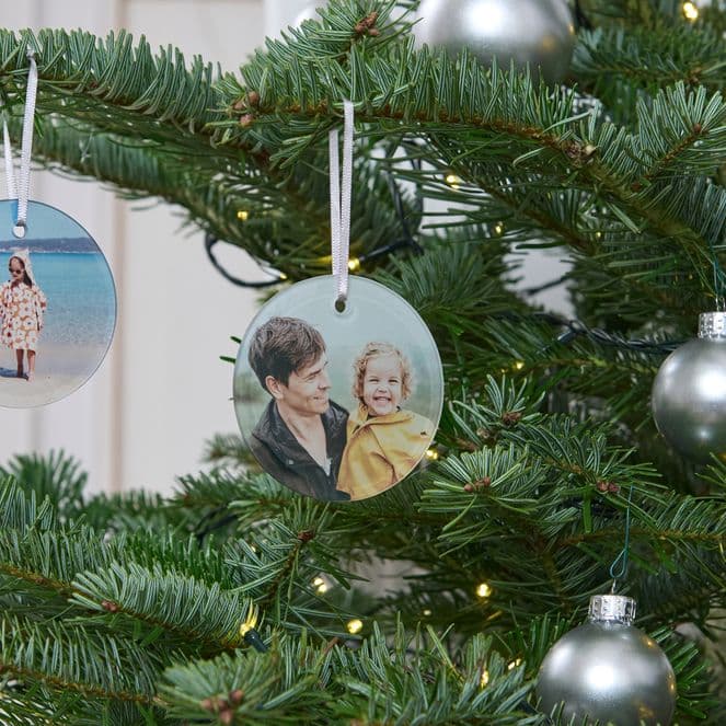 Christmas tree with silver baubles and personalized photo ornaments featuring people, a child, and a dog.