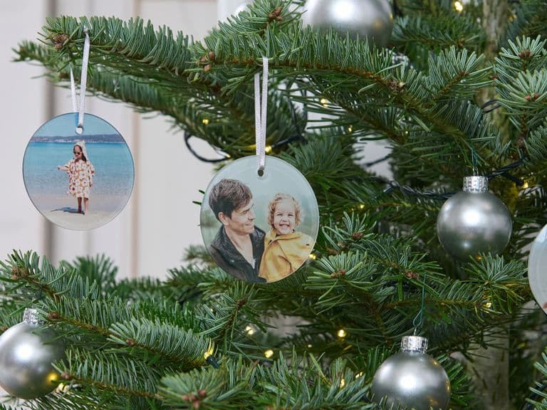 Christmas tree with silver baubles and personalized photo ornaments featuring people, a child, and a dog.