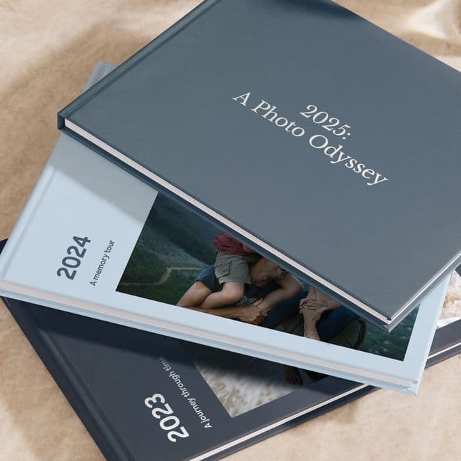 Three photo books titled "2023," "2024," and "2025: A Photo Odyssey" are stacked on a marble surface.