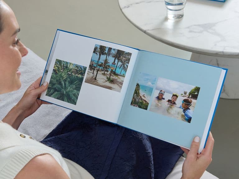 A woman holds a Popsa Photo Book with a blue cover