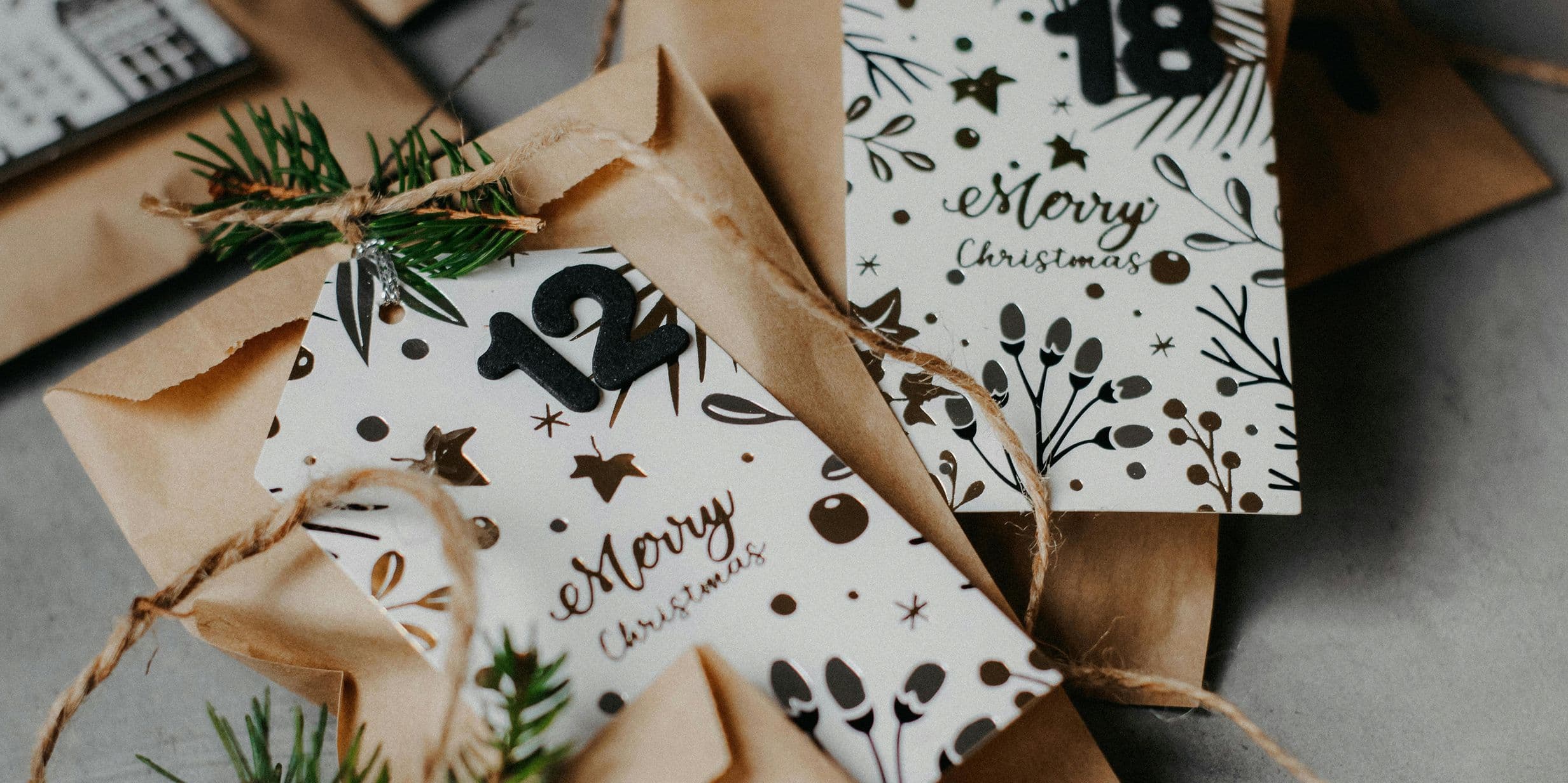 Festive envelopes with "Merry Christmas" cards, adorned with pine sprigs and twine, featuring numbers 12 and 18.