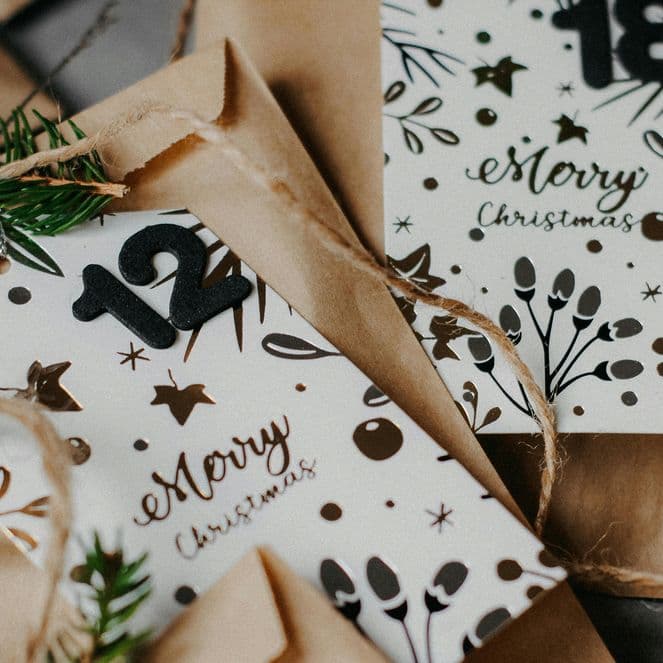 Festive envelopes with "Merry Christmas" cards, adorned with pine sprigs and twine, featuring numbers 12 and 18.
