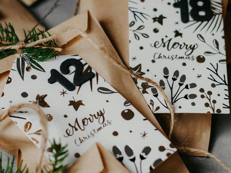 Festive envelopes with "Merry Christmas" cards, adorned with pine sprigs and twine, featuring numbers 12 and 18.