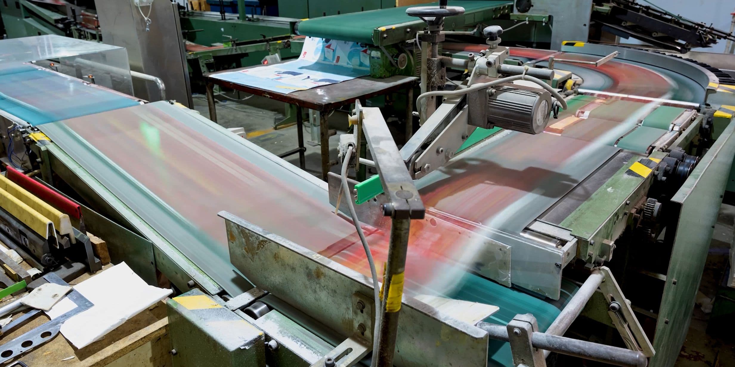 A factory conveyor belt system in motion, transporting printed materials through various machinery in an industrial setting.