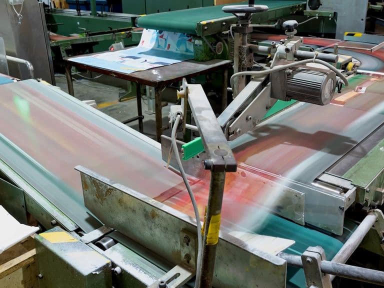 A factory conveyor belt system in motion, transporting printed materials through various machinery in an industrial setting.