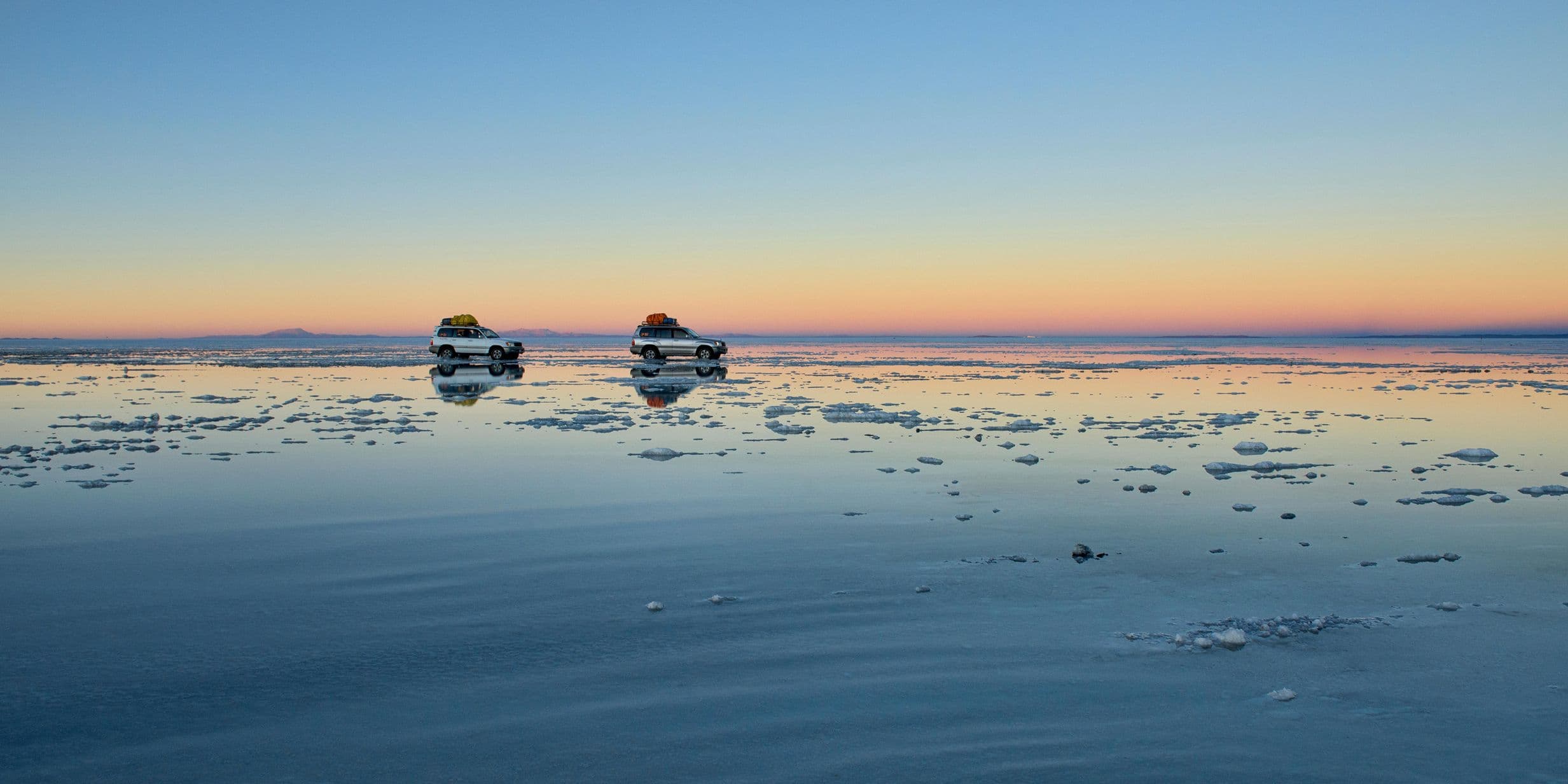 Two touring cars drive across salt flats, Uyuni, Bolivia