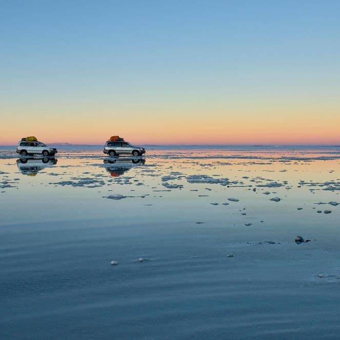 Two touring cars drive across salt flats, Uyuni, Bolivia