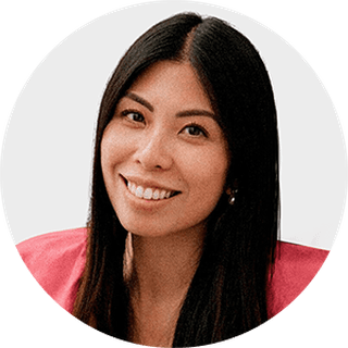 Smiling woman with long dark hair, wearing a pink top, against a plain background.