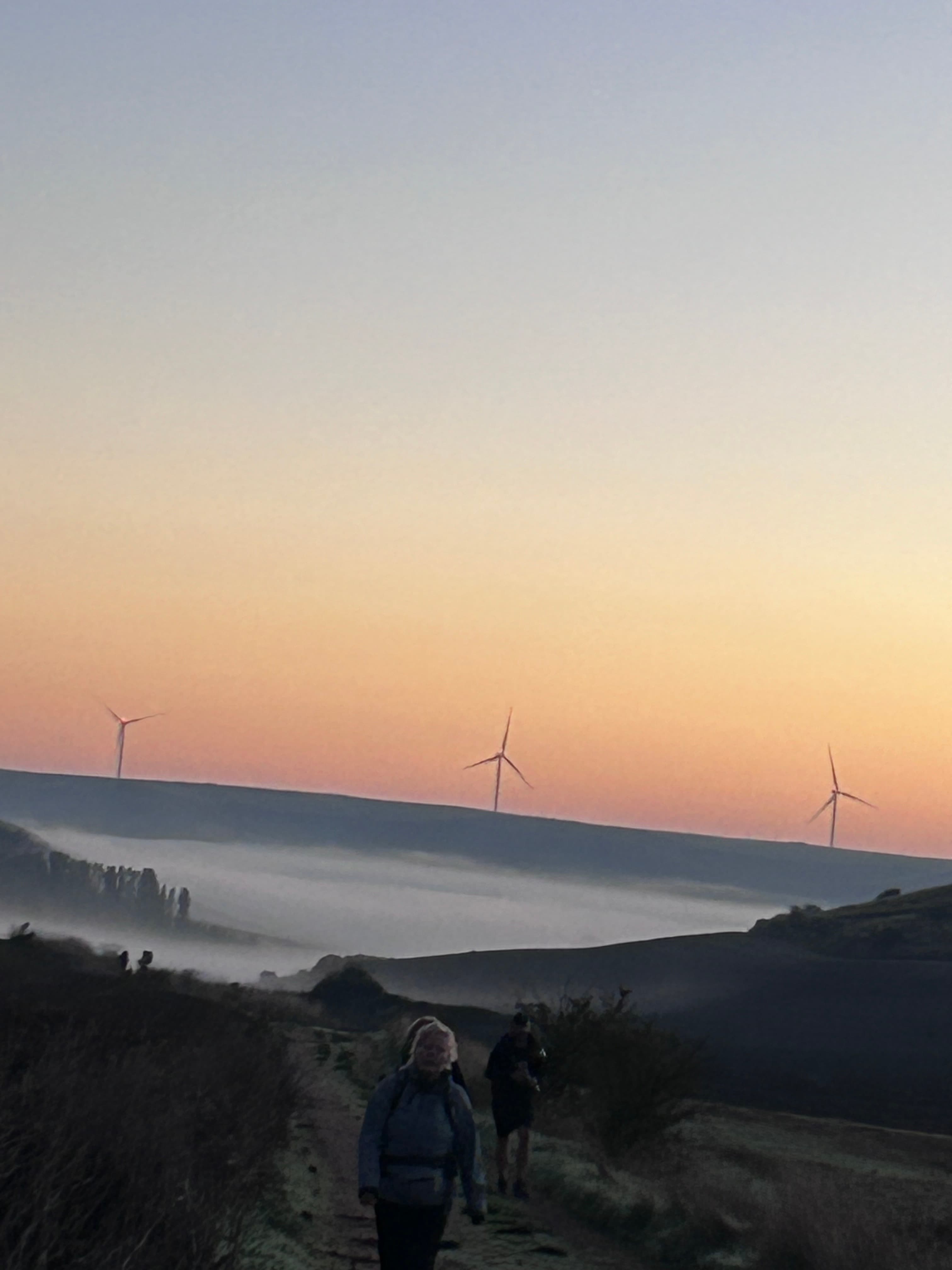 Wind turbines in the distance behind a group of hikers at sunset